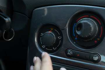 Fototapeta premium Woman hand reaches for the air conditioning mode knob on the panel in the car