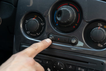 A man reaches for the button on the panel in the car with his finger to turn on the automatic mode of the air conditioner