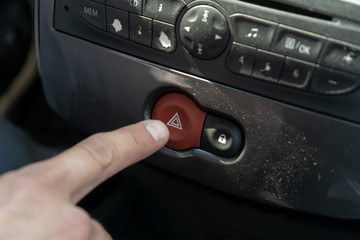 Fototapeta premium A man reaches for the button on the panel in the car with his finger to turn on the emergency gang