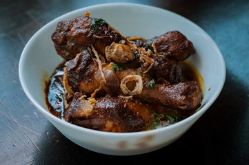 Malaysian dish of Ayam Masak Kicap or deep fried chicken in black soy gravy in a white bowl.