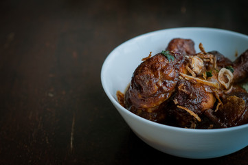 Malaysian dish of Ayam Masak Kicap or deep fried chicken in black soy gravy in a white bowl.