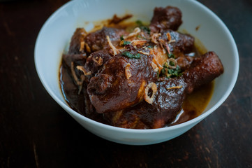 Malaysian dish of Ayam Masak Kicap or deep fried chicken in black soy gravy in a white bowl.