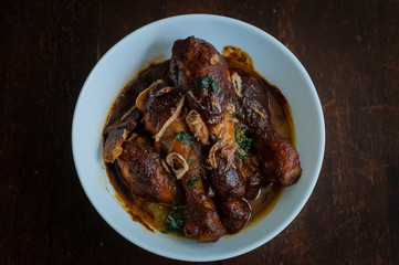 Malaysian dish of Ayam Masak Kicap or deep fried chicken in black soy gravy in a white bowl.