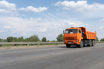 Fototapeta na wymiar Orange garbage truck on the road against the blue cloudy sky on the summer day