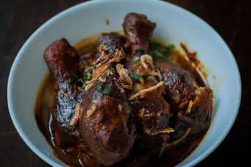 Malaysian dish of Ayam Masak Kicap or deep fried chicken in black soy gravy in a white bowl.