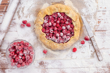 Homemade fruit pie (galette) made with fresh raspberries with powdered sugar on wooden table. Open pie, raspberry tart. Summer berry dessert. Flat lay.