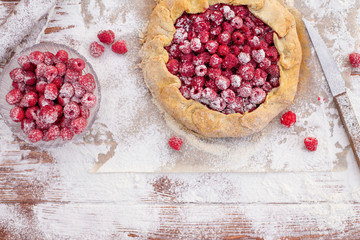Homemade fruit pie (galette) made with fresh raspberries with powdered sugar on wooden table. Open pie, raspberry tart. Summer berry dessert. Flat lay. Empty space for text, copyspace.