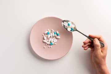 Hand with spoon of pills and plate with pills. Flat lay