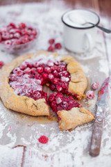 Homemade fruit pie (galette) made with fresh raspberries with powdered sugar on wooden table. Open pie, raspberry tart. Summer berry dessert.