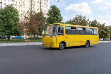 Yellow minibus rides on the paved city highway. The bus driver carries passengers along the route on a summer day