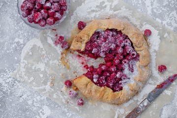 Homemade fruit pie (galette) made with fresh raspberries with powdered sugar on concrete background. Open pie, raspberry tart. Summer berry dessert. Flat lay. Empty space for text, copyspace.