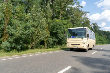 A minibus rides on an asphalt intercity highway through the forest. The bus driver carries passengers along the route on a summer day