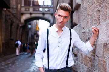 young European guy in shirt and trousers with suspenders walking around city