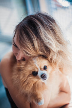Close up portrait of smiling young attractive woman embracing Pomeranian spitz.