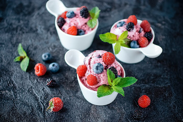 Three white cups with homemade popsicles made from fresh berries on a black background.