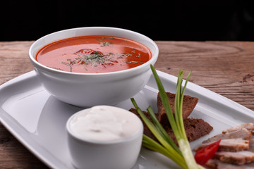 Ukrainian borsch with sour cream, onions and bacon on a white plate