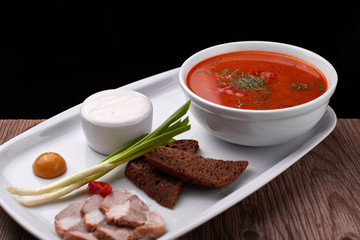 Ukrainian borsch with sour cream, onions and bacon on a white plate