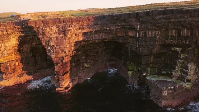 AERIAL DOLLY LEFT Impressive rock shelter formed by the sea waves erotion under a cliff at sunset