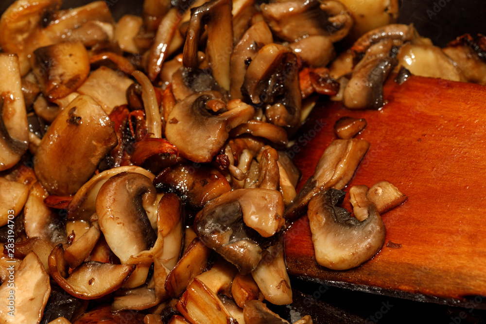 Wall mural Fried champignon mushrooms in a pan closeup background texture