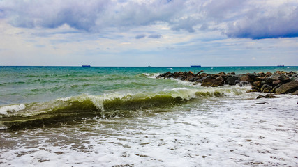 Stormy sea and large stones on the shore on a cloudy summer day with cumulus clouds on the sky.