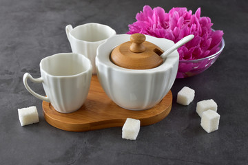 A nice teahouse composition of two empty cups, a sugar bowl and a peony flower on a concrete tabletop side view