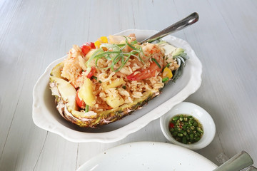 Closeup on Baked rice with pineapple served in a pineapple with chili fish sauce on white plate and white wooden table background.