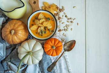 Pumpkin creamy soup served in individual pots, top view. Spoon and bread slice. Delicious colourful orange pumpkin soup for the cold fall weather with scattered pumpkin seeds. Rustic dinner table.