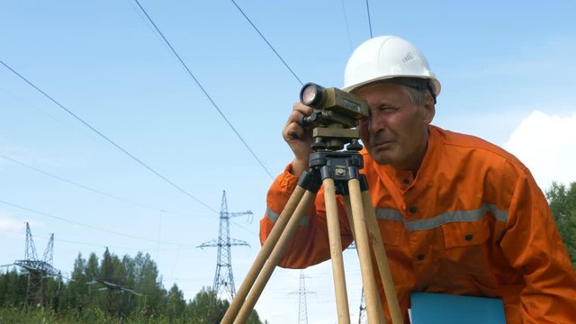 aged surveyor looks through dumpy level under power lines