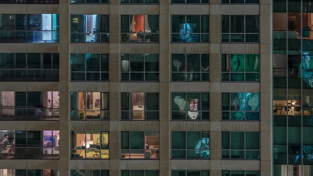 Glowing windows of the multi-storey building with lighting inside and moving people in apartments timelapse. Aerial view of modern residential skyscrapers in Dubai greens district