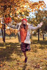 girl in red cap jumps with an autumn bouquet of leaves