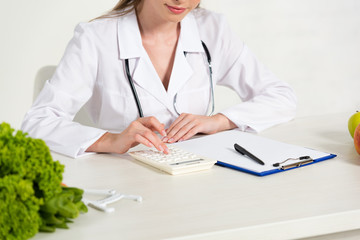 cropped view of dietitian using calculator at workplace
