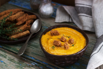 Pumpkin or carrot cream soup with croutons and thyme on a wooden background. Rustic style.