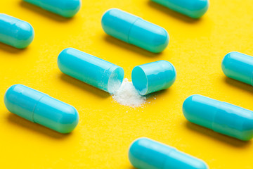 Blue tablets in capsules. One capsule is open. Yellow background.