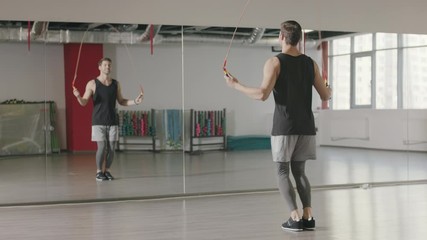Athlete man jumping on skipping rope at cardio training in gym club.