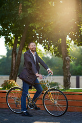 Obraz premium Bearded Businessman in business suit riding on retro bicycle to work on urban street in the morning on sunset