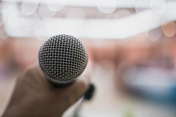 Speaker holding microphone for speaking, presentation on stage in public conference seminar hall with light background. Business meeting and education in teaching classroom concept