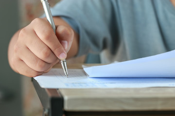 Education test exam in school concept : University student holding pen notes paper document sheet at lecture chair for taking exams in examination classroom. Assessment learning in class ideas