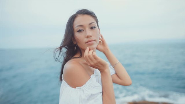 Woman stands by the ocean while looking straight at camera