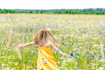 Little pretty girl in yellow Russian dress picking flowers in field of wild flowers on summer day.