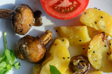on a white plate fried potatoes, mushrooms and tomato. Concept - Vegan Lunch