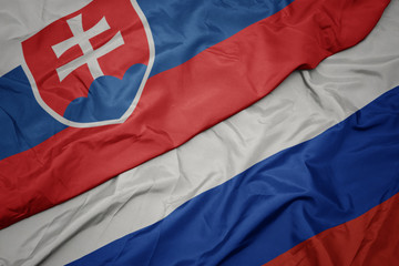 waving colorful flag of russia and national flag of slovakia.