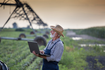 Farmer with laptop in front of irrigation system in field - obrazy, fototapety, plakaty