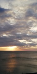 Fototapeta premium The autumn severe dark sea is illuminated by the setting sun, peeking through dense blue-gray clouds. Alarming and beautiful seascape. Dark gray clouds, solemn majestic sea and the golden setting sun.