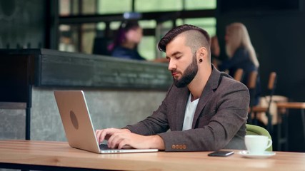 Handsome trendy male businessman chatting online using computer pc sitting on table at cafe