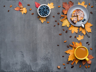 Seasonal autumn background. Frame of colorful maple leaves and a cup of hot drink, coffee, latte or cappuccino, nutmeg, cake, blueberries and cinnamon over grey.