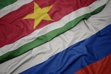 waving colorful flag of russia and national flag of suriname.