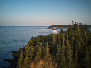 Aerial drone image of the Owls head Lighthouse surrounded by pristine forest on the cliffs overlooking the entrance to Owls Head Harbor on the Maine Coast at sunset