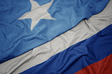 waving colorful flag of russia and national flag of somalia.