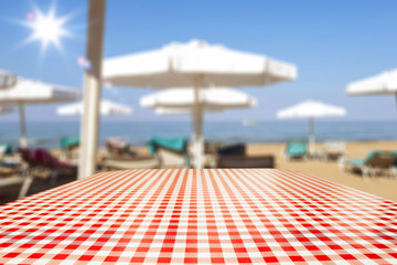 Table background with beach umbrellas and sun beds in distance. Empty space for advertising products and decoration.