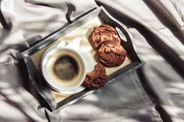 Female hand holds a cup of coffee on the bed with light linen in a room with natural sunlight and shadow, top view flat lay